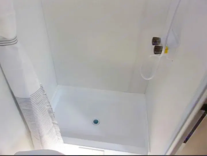 Inside an RV rental: a compact, bright white shower stall with a striped curtain and shower controls.. Forest River Salem FSX  164RBLE 2024