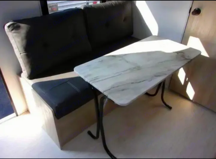 Compact RV rental dinette with a dark upholstered bench and a modern marble-look table, brightly lit by sunlight.. Forest River Salem FSX  164RBLE 2024