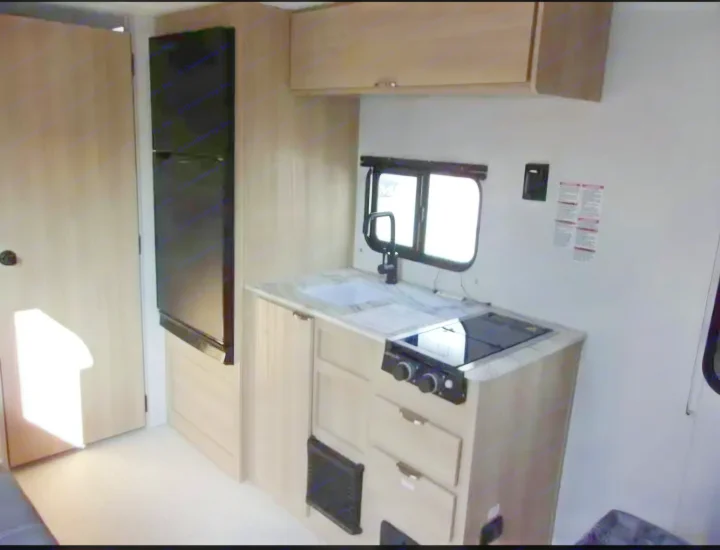This RV rental features a compact kitchen with light wood cabinetry, a sink, cooktop, and refrigerator on the left.. Forest River Salem FSX  164RBLE 2024