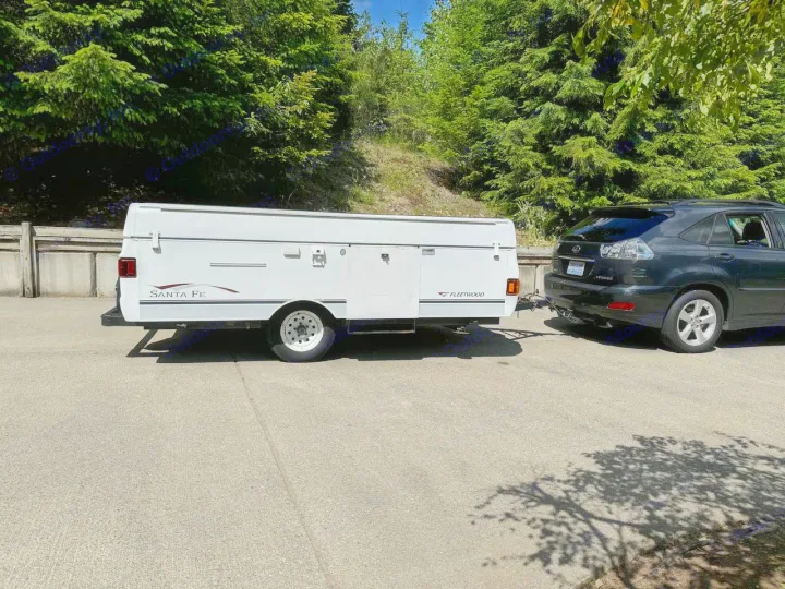 A white Fleetwood Santa Fe pop-up camper is hitched to a black SUV, ready for an rv rental trip.. Fleetwood Santa Fe 2004
