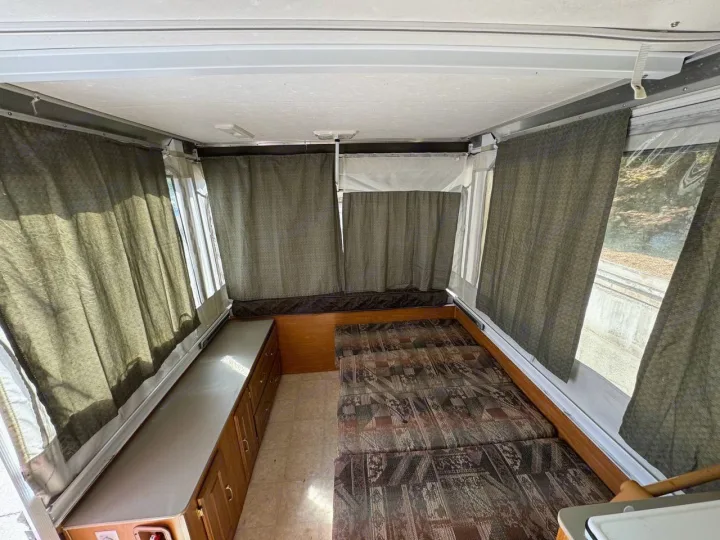 View inside an RV rental pop-up camper, showing comfortable beds, bright windows with privacy curtains, and storage.. Fleetwood Santa Fe 2004