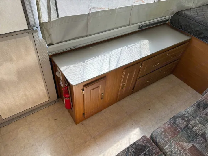 Pop-up RV rental interior: wooden storage cabinet, countertop, and a mounted fire extinguisher for safety.. Fleetwood Santa Fe 2004