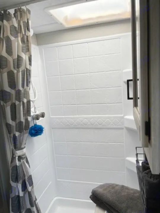 Clean RV rental shower featuring a patterned curtain, skylight, and white tiled walls for a comfortable travel experience.. Forest River Aurora Aurora 2024