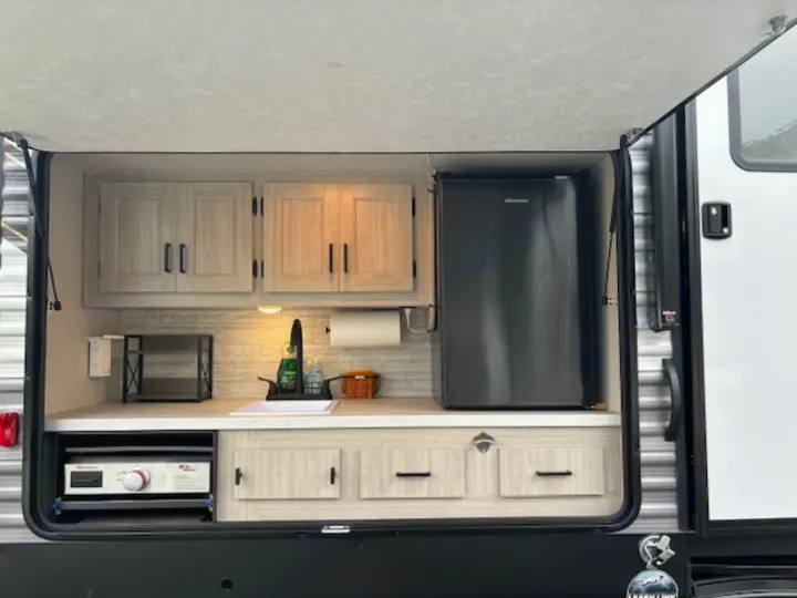 Explore this RV rental's outdoor kitchen! Features include a sink, fridge, pull-out griddle, and ample storage for camping.. Forest River Aurora Aurora 2024