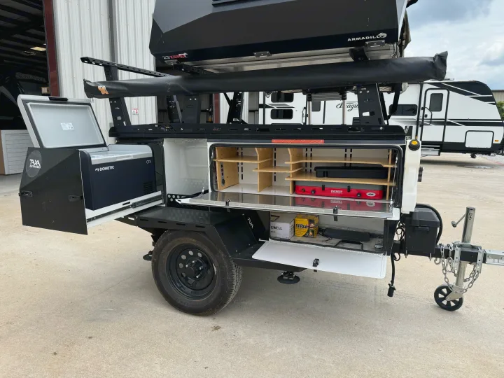 Compact RV rental trailer featuring an open outdoor kitchen with Dometic fridge, camp stove, and rooftop tent.. taxa Woolly Bear 2017