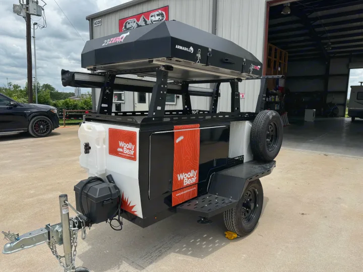 A sleek black and white Woolly Bear off-road utility trailer, topped with a 23ZERO rooftop tent, is shown, ideal for rv rental.. taxa Woolly Bear 2017