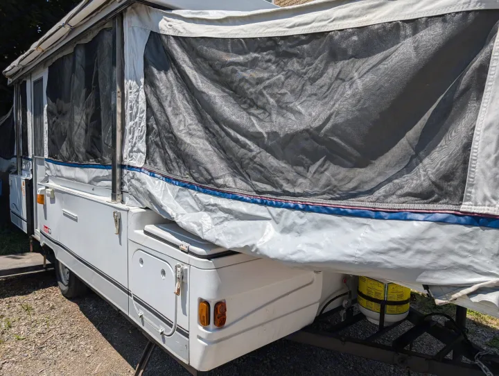 White pop-up camper RV rental with mesh windows and propane tank, ideal for camping adventures.. Coleman Utah 2003