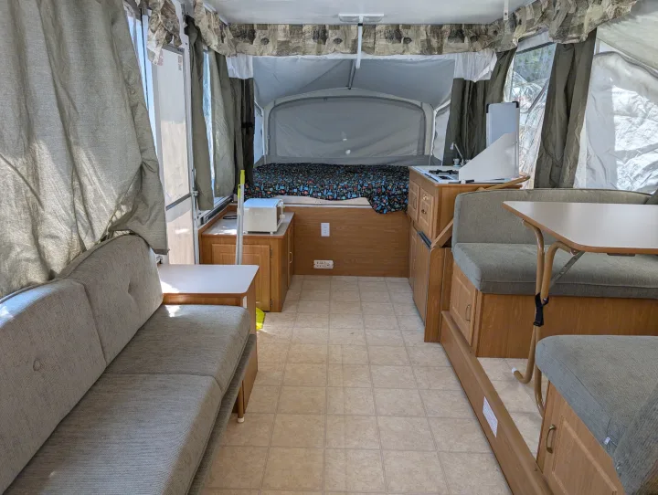Interior of an RV rental pop-up camper featuring a bed, kitchenette, dinette, and comfortable sofa seating.. Coleman Utah 2003