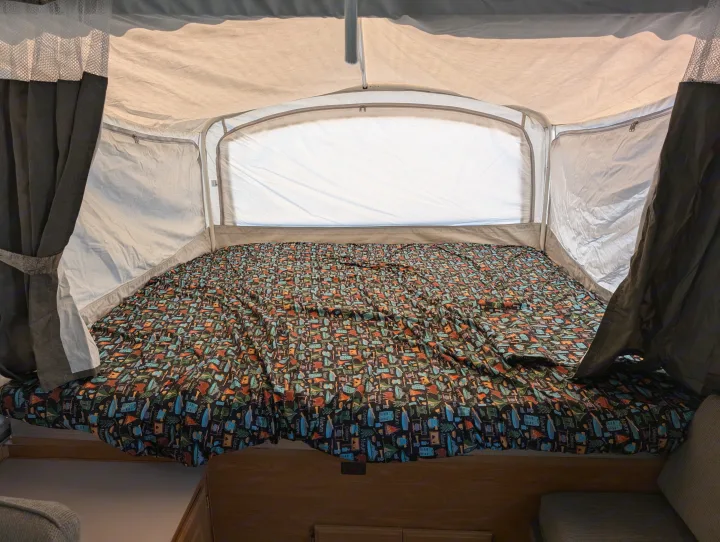 Cozy pop-up camper bed in an RV rental, featuring vibrant camping-themed bedding and interior tent walls with curtains.. Coleman Utah 2003