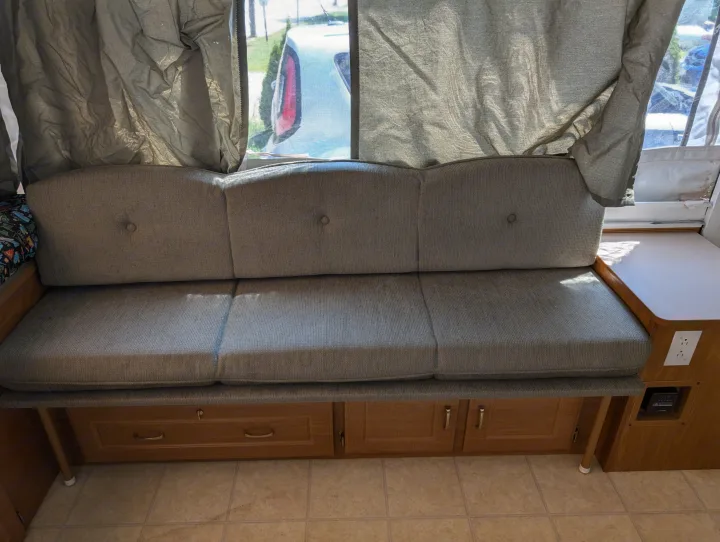 Comfortable grey bench seating in an RV rental, featuring button-tufted backrests, under-seat storage, and a view outside.. Coleman Utah 2003