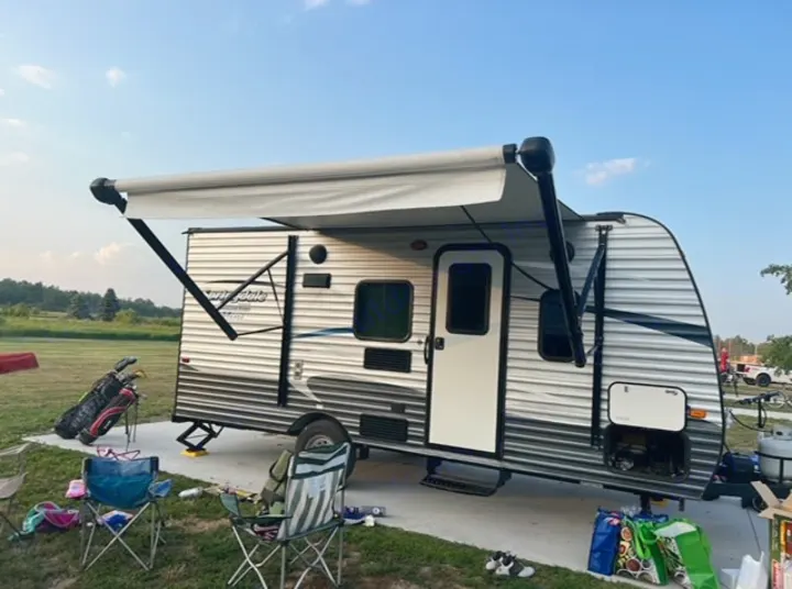 This RV rental, with its awning extended, is ready for relaxation at a sunny campsite, complete with camping chairs and golf clubs.. Keystone RV Summerland Mini 2017