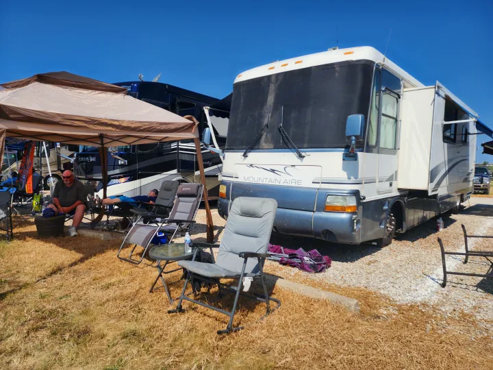 Outdoor relaxation at an RV rental campsite. A Mountain Aire RV is parked, with people relaxing under a canopy.. Newmar Mountain Aire 1998