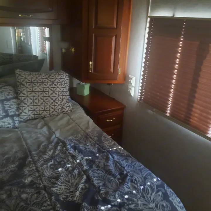 Cozy RV rental bedroom featuring a bed with patterned bedding, wooden cabinets, and blinds, perfect for your next adventure.. Newmar Mountain Aire 1998