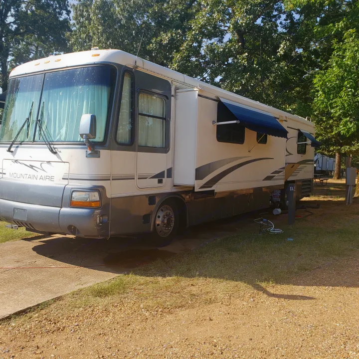 White & gray Mountain Aire RV, a perfect rv rental choice, parked at a sunny campsite with blue awnings extended.. Newmar Mountain Aire 1998