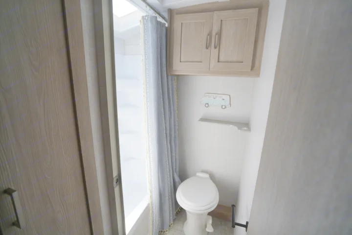 This RV rental's compact bathroom includes a shower, toilet, overhead cabinets, and a decorative shelf for your travels.. Forest River Rockwood 2021