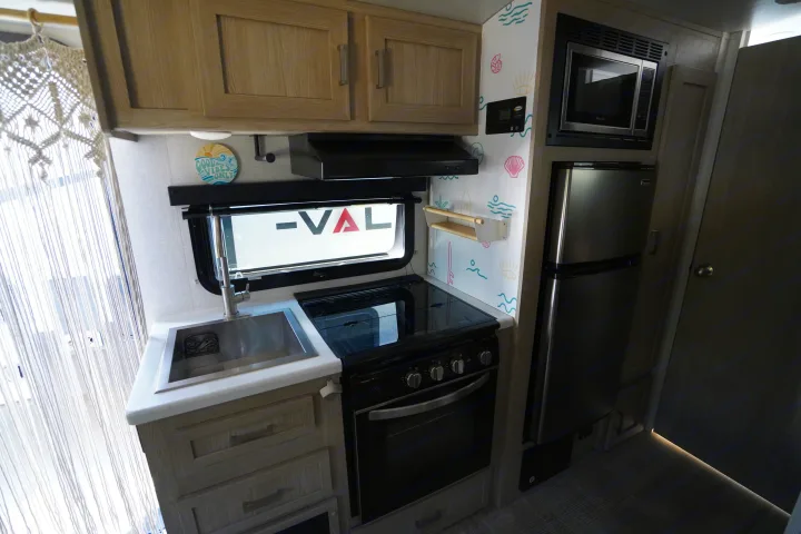 This RV rental's compact kitchen boasts a sink, stove, microwave, fridge, light wood cabinets, and vibrant, beach-themed decor.. Forest River Rockwood 2021