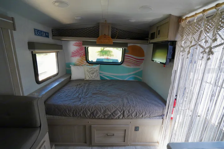 Relaxing rv rental bedroom featuring a beach-themed mural, cozy bed, macrame decor, and window views. Ideal for travel.. Forest River Rockwood 2021