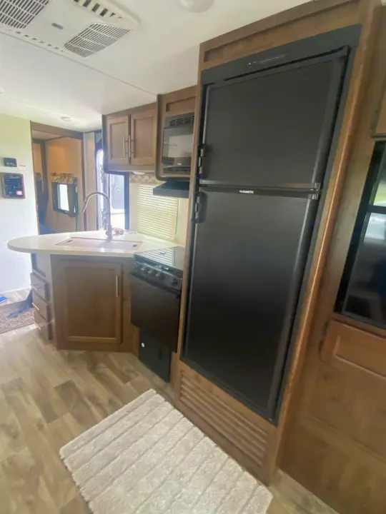 Spacious RV rental kitchen with modern fridge, sink, stove, microwave, and ample cabinets. Features wood-look flooring and bright interior.. Keystone Cougar Half-Ton 2018