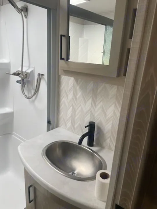 Modern RV rental bathroom showcasing a shower, sink, sleek black faucet, mirror, and stylish chevron backsplash.. Forest River Rockwood Ultra Lite 2022