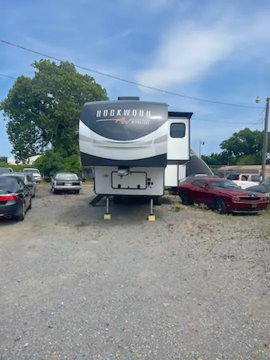A large, modern Rockwood fifth-wheel RV, white with black accents, is parked on a gravel lot. Consider this for your next rv rental!. Forest River Rockwood Ultra Lite 2022