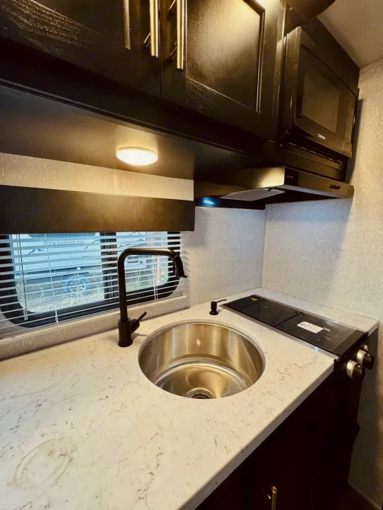 Inside our RV rental: a functional kitchen featuring a stainless steel sink, cooktop, microwave, and stylish dark cabinetry.. Forest River Cherokee Wolf Pup 2022
