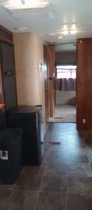 RV rental interior: kitchen with fridge and trash, leading to a carpeted bedroom. Features AC unit & tiled floor.. Keystone Hideout 2015