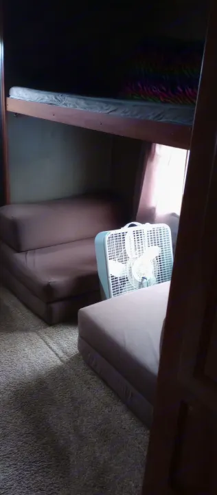 Inside an RV rental: bunk beds above a foldable sofa and a fan on the carpeted floor, offering a functional sleeping area.. Keystone Hideout 2015