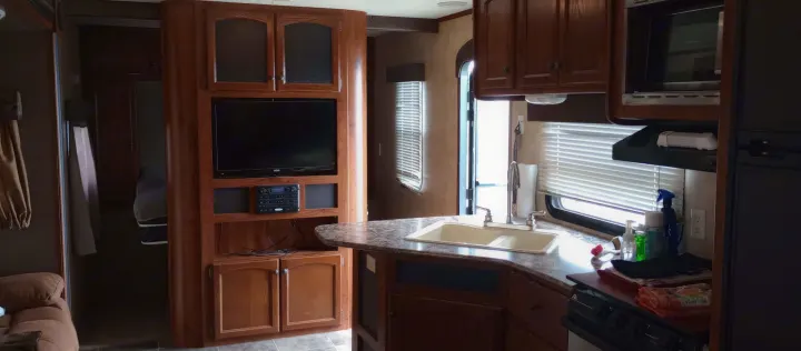 RV rental interior with a fully equipped kitchen, entertainment center, and glimpse into the bedroom.. Keystone Hideout 2015