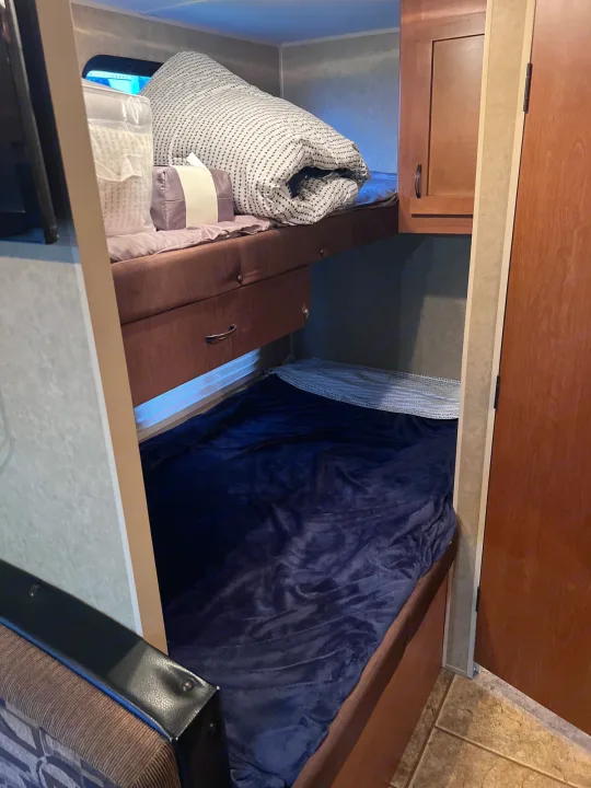 RV rental bunk beds: The upper bed has folded patterned bedding, a packaged pillow & purple pillow. Lower bed with dark blue blanket.. Forest River Cherokee Grey Wolf 2013