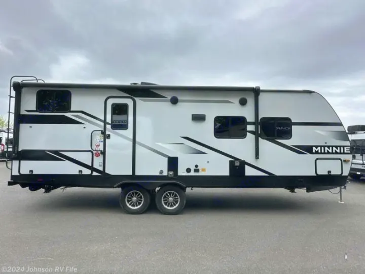 Side view of a white travel trailer, perfect for an rv rental. Modern camper with black/gray graphics, entry door, windows, and two axles.. Winnebago Minnie 2301BHS 2024