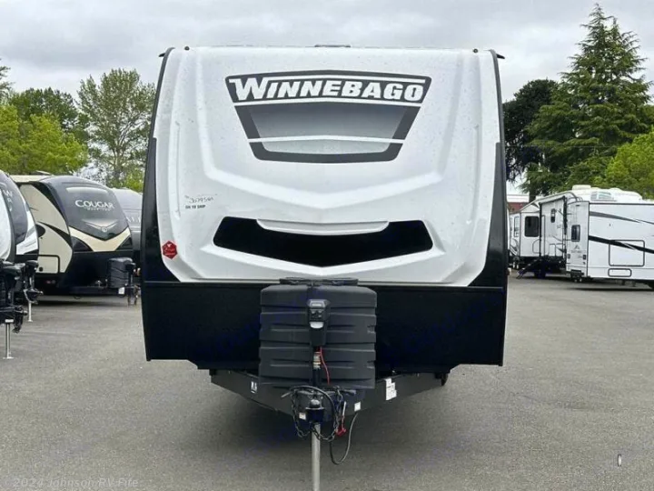 Front view of a white Winnebago travel trailer, ideal for an rv rental. Propane tanks visible in a paved lot with other RVs.. Winnebago Minnie 2301BHS 2024
