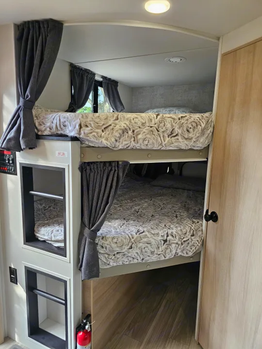 Modern rv rental interior features comfortable bunk beds with curtains, built-in storage, and a fire extinguisher.. Winnebago Minnie 2301BHS 2024
