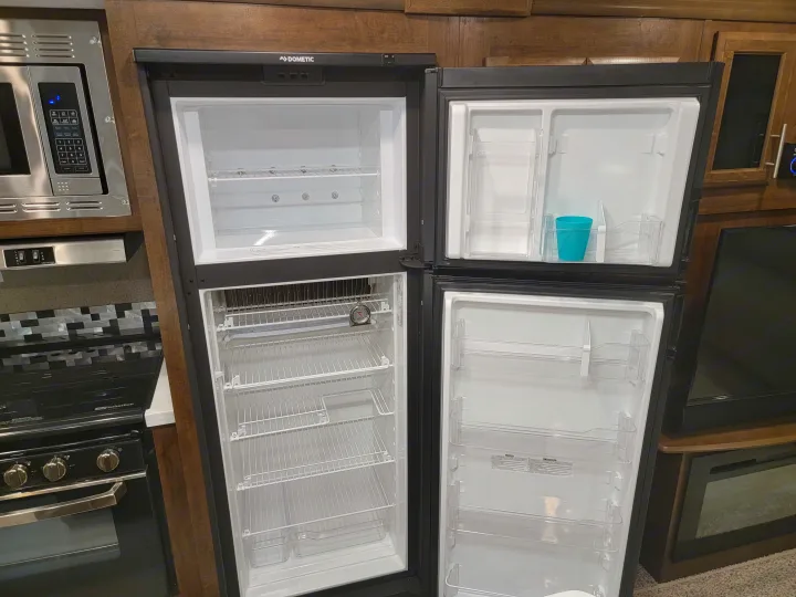 RV rental kitchen: Open Dometic fridge (mostly empty), microwave, Greystone hood, and Suburban stove. Compact layout.. Forest River Rockwood Signature 2020