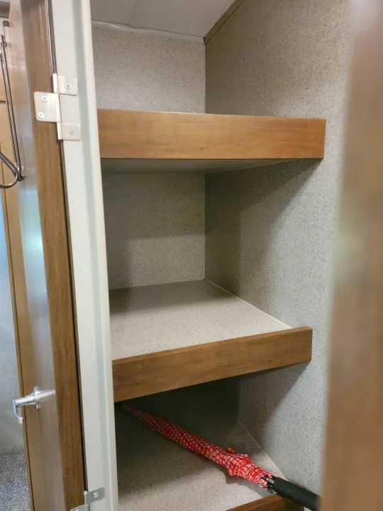 An RV rental closet with two wooden shelves, textured walls, and an umbrella, showing practical storage space.. Forest River Rockwood Signature 2020