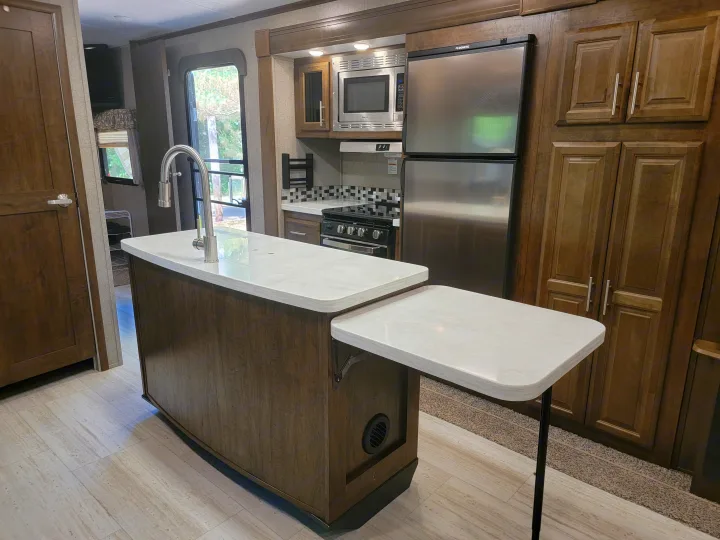 Modern RV rental kitchen featuring a large island, stainless steel appliances including a Dometic fridge, and extendable counter.. Forest River Rockwood Signature 2020