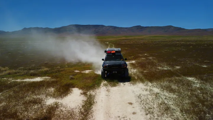 An overland vehicle creates a dust cloud while driving on a dirt trail through a vast, grassy plain. Explore with an RV rental!. Toyota Tacoma - GoFastCamper 2007