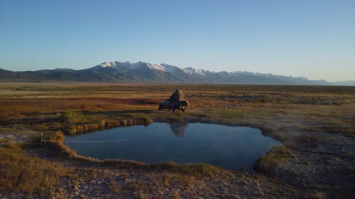 RV rental: A truck with a pop-up tent camps by a tranquil hot spring, reflecting snowy mountains and vast plains.. Toyota Tacoma - GoFastCamper 2007