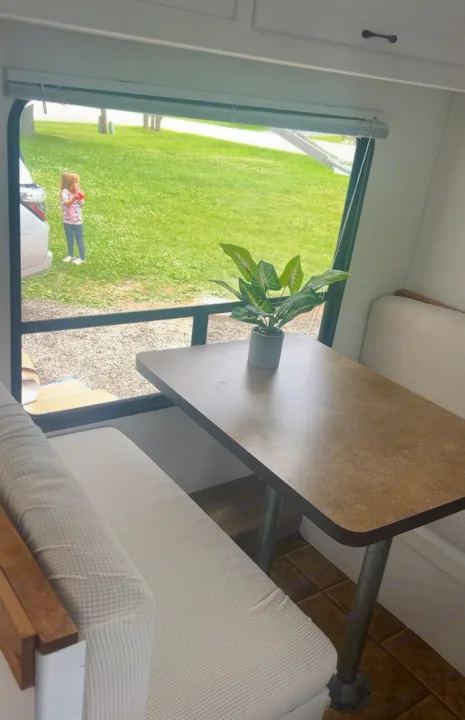 An RV rental's dinette area, featuring bench seating, a table with a plant, and a window view of a child playing in green grass.. Forest River Cherokee Grey Wolf 2012
