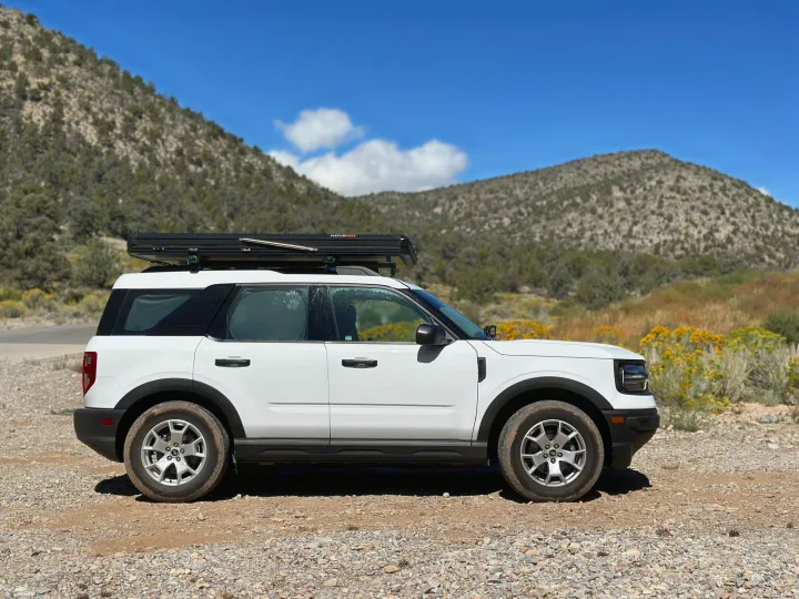 Scenic rv rental adventure: White Ford Bronco Sport with a NaturNest rooftop tent on a mountain trail.. Ford Bronco Sport 2022
