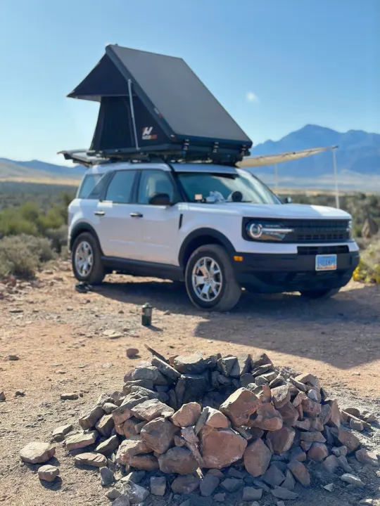 A white Ford Bronco Sport with a rooftop tent at a desert campsite, ready for adventure. A rugged RV rental alternative!. Ford Bronco Sport 2022