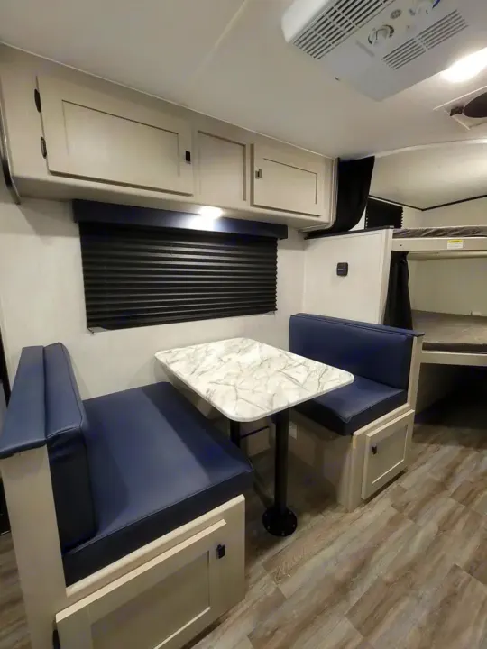 This spacious RV rental features a dinette with blue cushions, overhead storage, and rear bunk beds, perfect for family travel.. Coachmen Apex Nano 2024