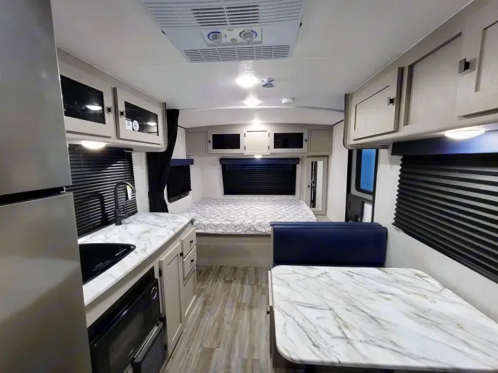 This modern RV rental interior features a compact kitchen with marble-look counters, a dinette, and a comfortable rear bed.. Coachmen Apex Nano 2024