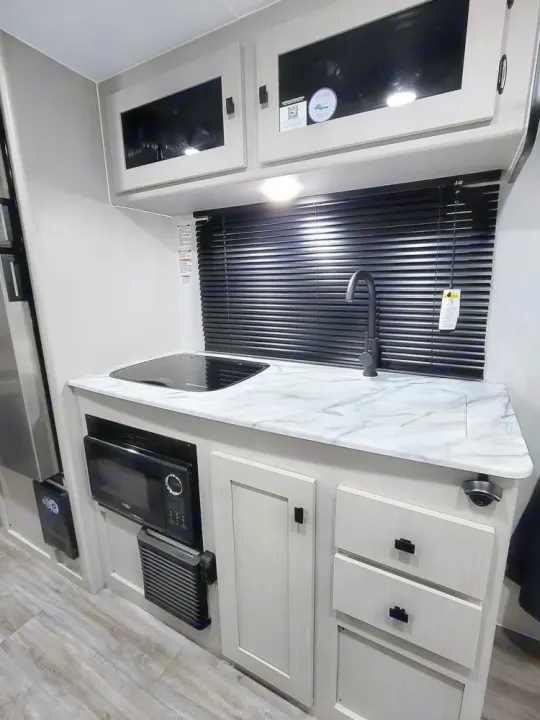 RV rental: Bright kitchenette with light cabinets, marble counter, sink, stovetop, microwave, and black blinds.. Coachmen Apex Nano 2024
