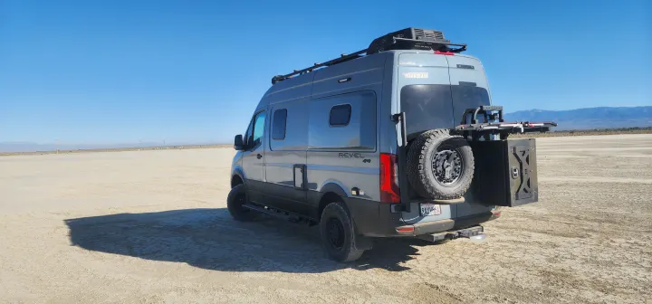 A gray Revel 4x4 camper van, perfect for an rv rental adventure, parked on a wide desert playa under a clear blue sky.. Winnebago Revel 2022