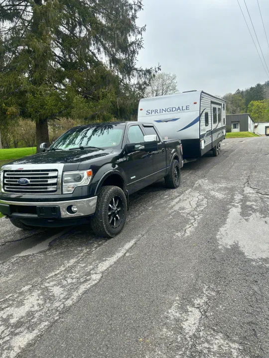 Black Ford F-150 pickup truck towing a white Springdale RV, parked on a paved road. Perfect for your next RV rental adventure.. Keystone RV Springdale 2021