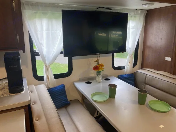 Inside an RV rental: a modern dinette with light gray benches, table set with green plates/cups, TV, & coffee maker.. Georgetown GT3 2016