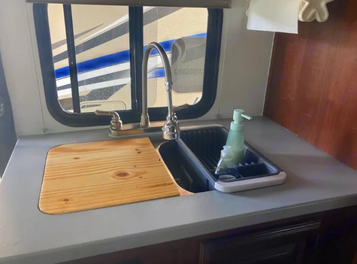 RV rental kitchen with gray counter, sink, cutting board, and faucet. Features soap dispenser and window view of another RV.. Georgetown GT3 2016