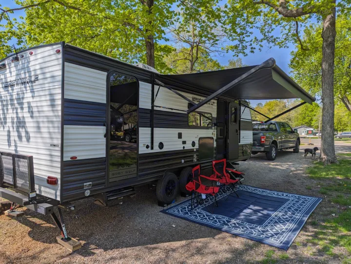 Relaxing RV rental setup at a shaded campsite, featuring an extended awning, chairs, rug, and truck.. Forest River Cherokee Grey Wolf 23DBH 2024