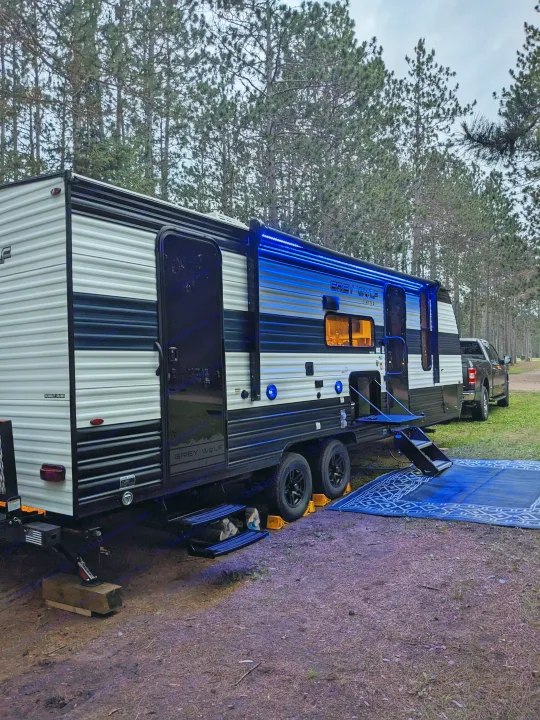 Spacious Grey Wolf RV rental with blue LED lights and outdoor mat, perfectly set up in a serene forest campsite.. Forest River Cherokee Grey Wolf 23DBH 2024
