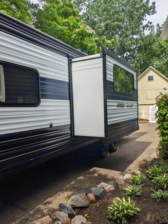 This Grey Wolf travel trailer with extended slide-out is ideal for your next RV rental adventure, parked on pavement next to a garden.. Forest River Cherokee Grey Wolf 23DBH 2024